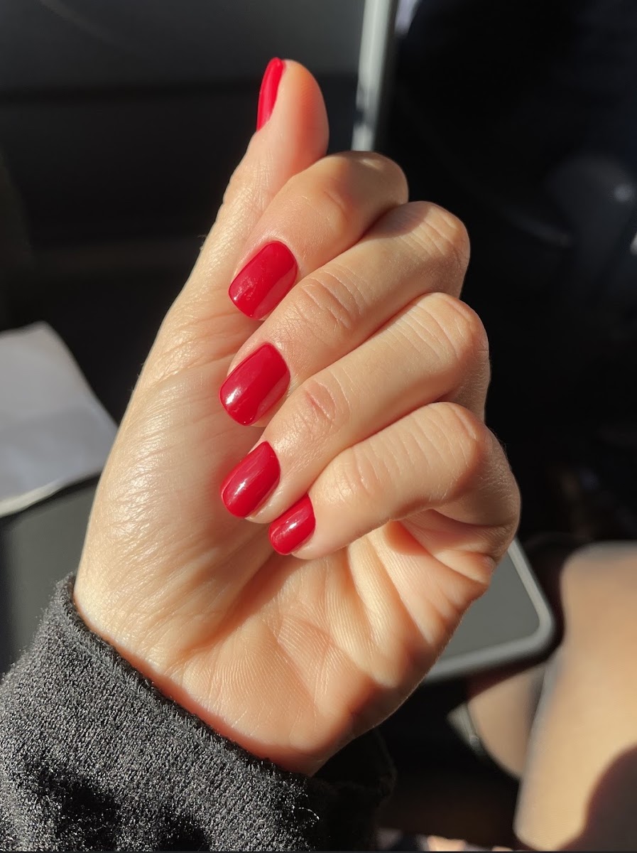 Mano con uñas cortas pintadas en rojo brillante sobre el volante de un coche
