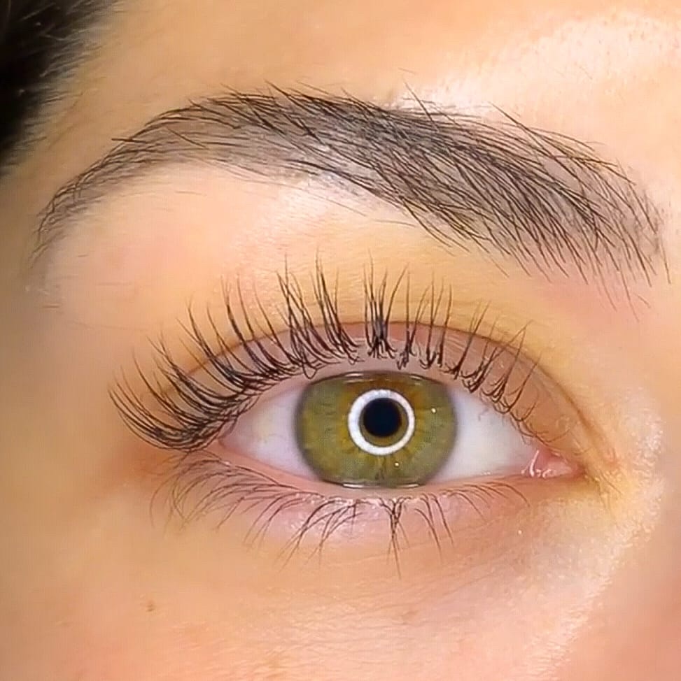 Primer plano de un ojo con extensiones de pestañas, la ceja peinada y la pupila verde
