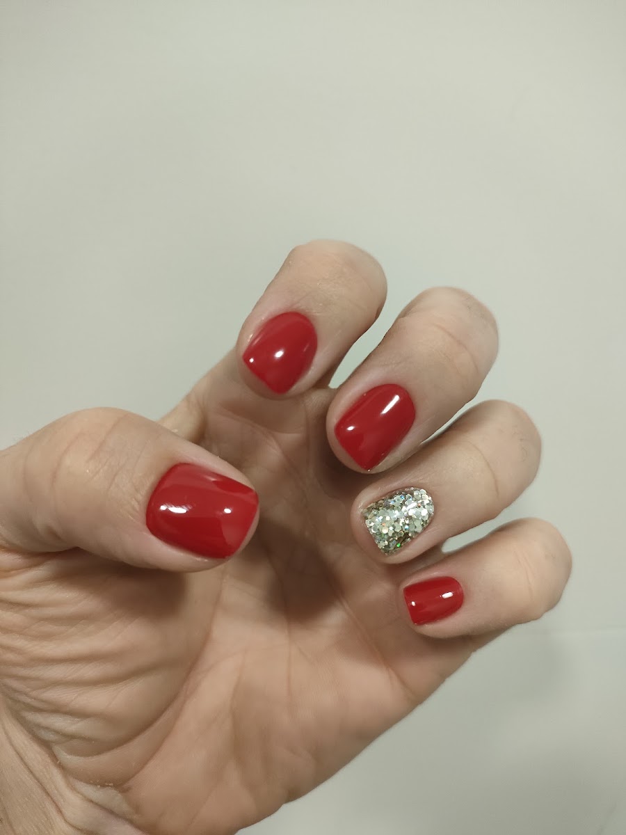 Mano con uñas rojas brillantes y una uña dorada con purpurina sobre fondo blanco